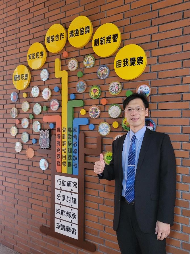 陳賢璁校長於校園意象牆前合影,牆上展示著團隊合作、溝通協調、創新經營等教育核心價值。